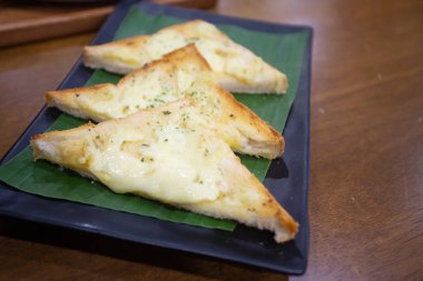 Peynirli sarımsaklı ekmek parçalara bölünmüş, tabağa konmuş.