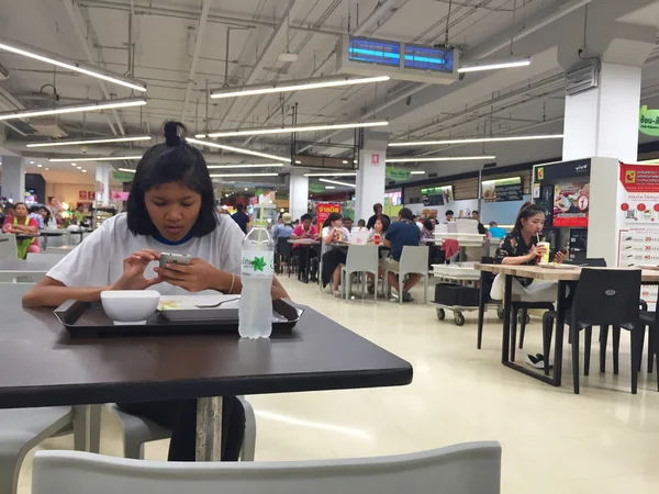 BANGKOK, TAILANDIA - 10 DE OCTUBRE: Mujer no identificada comiendo y usando teléfono móvil dentro de la supertienda Big C el 10 de octubre de 2016 en Bangkok, Tailandia —  Fotos de Stock
