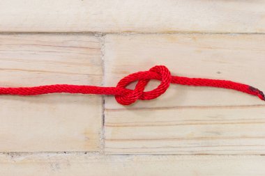 Ahşap arka plan üzerinde kırmızı iple yapılan sekiz rakamı şeklindeki düğüm