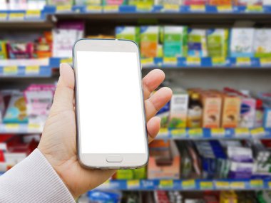Sol Asya el ile çeşitli marka tıp hapları ve takviyeleri eczane stand bulanık arka plan üzerinde boş ekran akıllı telefon tutarak kazak.