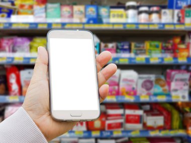 Sol Asya el ile çeşitli marka tıp hapları ve takviyeleri eczane stand bulanık arka plan üzerinde boş ekran akıllı telefon tutarak kazak.