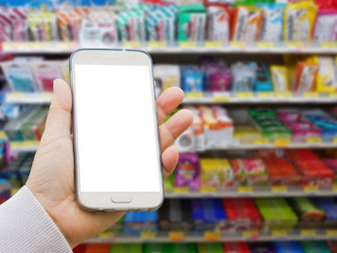 Sol Asya el ile çeşitli marka pastil ve ambalaj Satılık süpermarket stand veya raf sakıza bulanık arka plan üzerinde boş ekran akıllı telefon tutarak kazak 