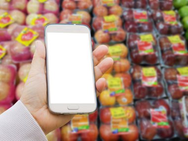 Asya eliyle sol raf süpermarkette satılan ambalaj içinde kırmızı elma bulanık arka plan üzerinde boş ekran akıllı telefon tutarak kazak 
