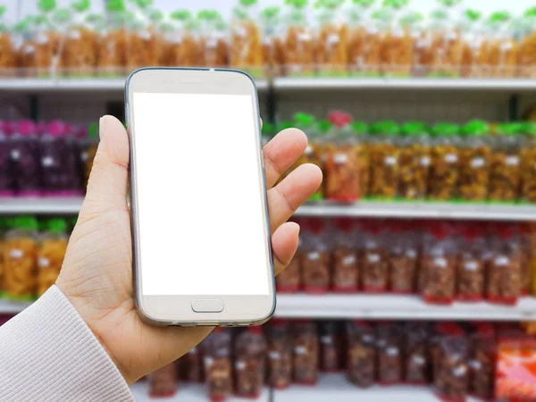 left asian hand with pullover holding smart phone on blurred background of snack made of agricultural products in packaging for sale on supermarket stand