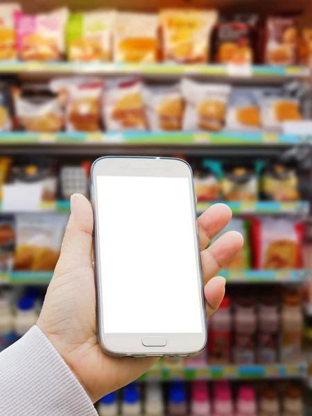 left asian hand with pullover holding blank screen smart phone on blurred background of various brand of burger and pasteurized milk in packaging for sale on supermarket stand or shelf