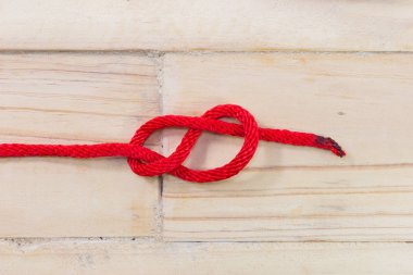 Ahşap arka plan üzerinde kırmızı iple yapılan sekiz rakamı şeklindeki düğüm