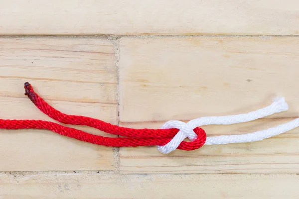 Bogen-Biegeknoten aus rotem Seil auf Holzgrund. — Stockfoto