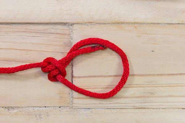 bowline knot made from red synthetic rope, tightening on wooden background.
