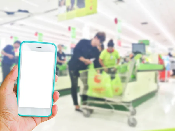 Sinistra che tiene il telefono cellulare verde dello schermo bianco con lo sfondo sfocato del supermercato, concetto di shopping online — Foto Stock