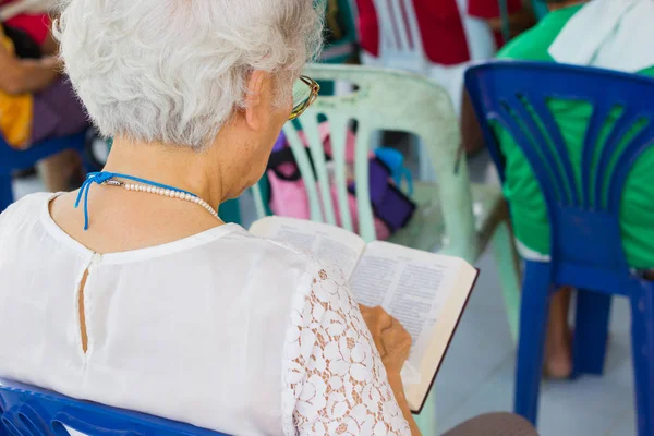 Gammal kvinna med vitt hår läsa Bibeln i en kyrka — Stockfoto