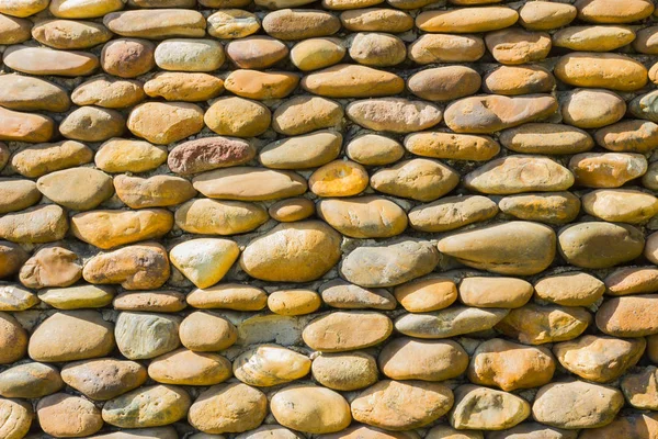River pebbles round stone wall background in sunshine — Stock Photo, Image