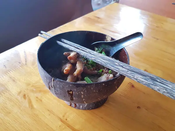 Fideos con patas de pollo en un tazón de concha de coco sobre fondo de madera —  Fotos de Stock