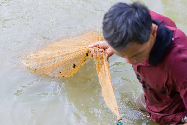 Chiang rai, thailand - 21. Mai 2017: Unbekannter Fischer in dunkelrotem Poloshirt zieht das Netz aus dem Teich in chiang rai, thailand. — Stockfoto