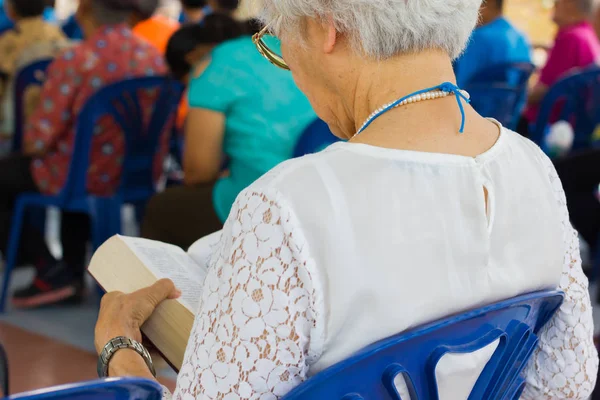 Anciana con el pelo blanco leyendo la santa Biblia en una iglesia — Foto de Stock