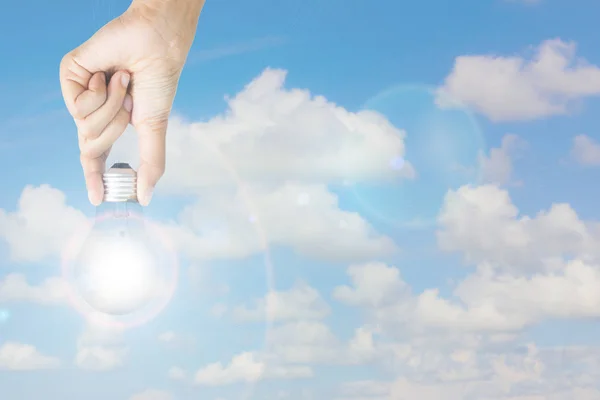 Hand from above holding light bulb with lens flare on blue sky background. Copyspace on the left. Eco power concept.