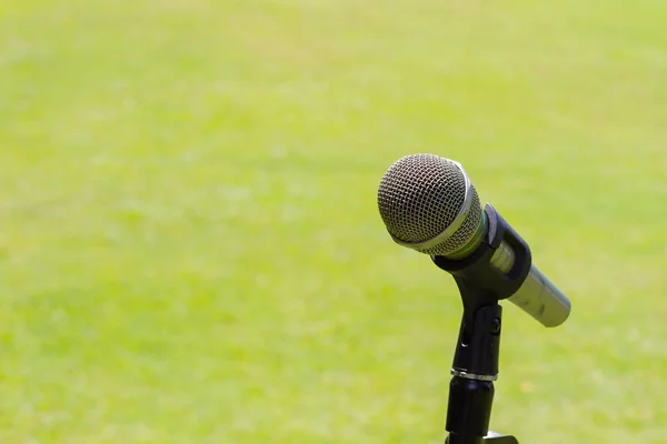 Microphone sur un stand avec fond de pelouse vert flou, Copyspace sur la gauche . — Photo