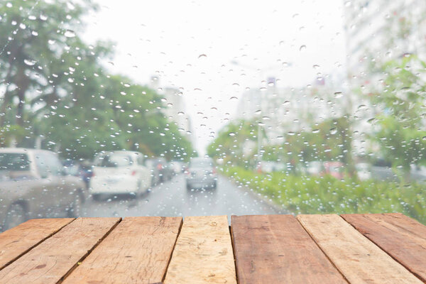 Wooden board empty table in front of blurred raining on the windshield of a vehicle on the street
