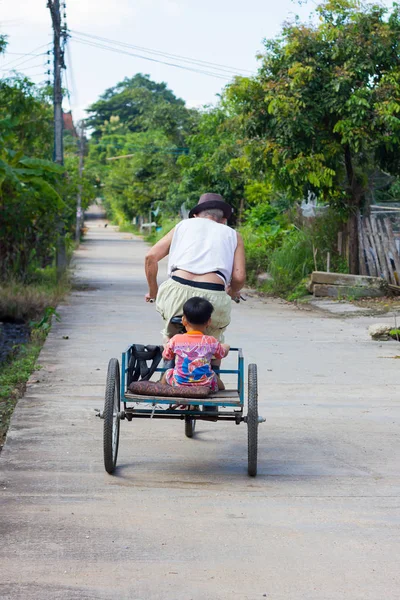 CHIANG RAI, THAILAND - NOVEMBRO 5: homem velho asiático deficiente não identificado montando triciclo na estrada com seu neto na parte de trás em novembro 5, 2017 em Chiang rai, Tailândia . — Fotografia de Stock