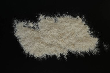 Küçük bir miktar beyaz un düz siyah bir yüzeye saçılmıştır. Gıda arkaplanı.