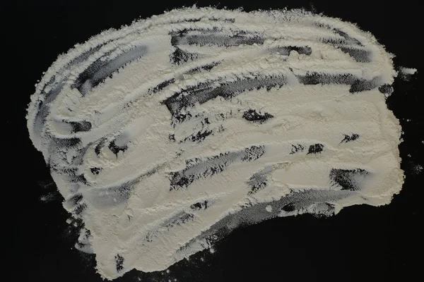 Egy kis mennyiségű fehér sütőliszt szétszóródik egy lapos fekete felületen. Élelmiszer-háttér. — Stock Fotó