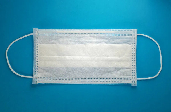 Mavi arka planda beyaz tıbbi maske. Virüs, grip, koronavirüs konsepti.