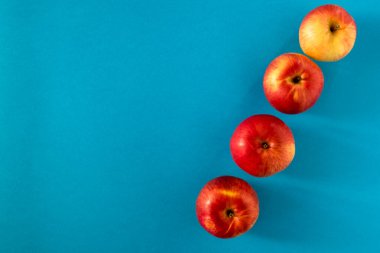 Dört sarı-kırmızı olgun elma çapraz olarak mavi bir yüzeye serilmiştir. Yukarıdan bak. Boşluğu kopyala.