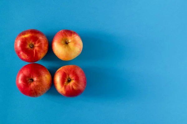 Four yellow-red ripe apples are laid out on a blue surface. View from above. Copy space.