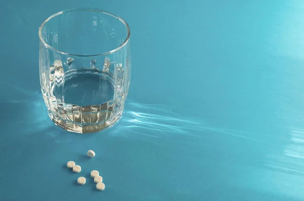 Um copo de água e alguns comprimidos brancos sobre um fundo azul. Conceito de medicina e farmacologia . — Fotografia de Stock