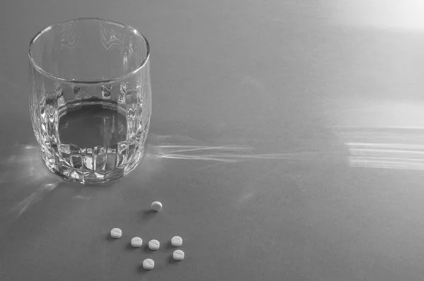 A glass of water and white tablets in a hard light on a blue background. Black and white. — Stock Photo, Image