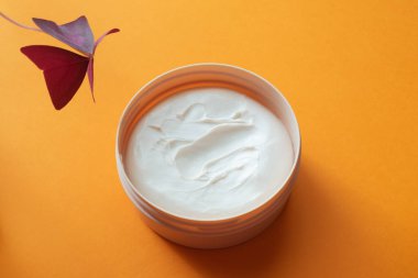 Turuncu arka planda yüz kremi ya da vücut ve ev yapımı bitki oksalis içeren kavanozu aç..