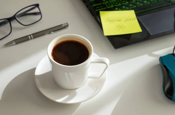 Une tasse de café sur le lieu de travail, un stylo, un ordinateur portable, des lunettes. Lumière dure. Café premier concept . — Photo