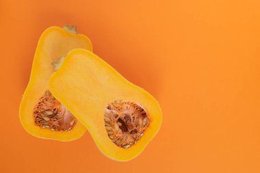 Tohumlarla dolu olgun, parlak bir balkabağı. İkiye bölünmüş ve turuncu bir arka planda yatıyor..