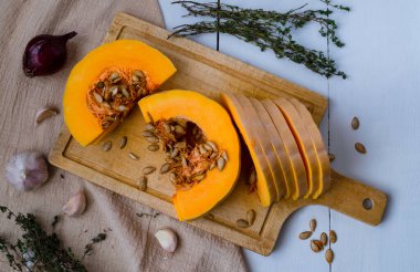 Olgun balkabağı parçaları, kekik, sarımsak, kırmızı soğan ve balkabağı tohumları ahşap kesim tahtasının üzerinde, pişirmek için pişirilmiş ya da basit, lezzetli ve sağlıklı bir yemek için. Sağlıklı beslenme bir kavramdır. Yatay yönelim.