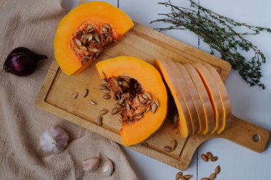 Olgun balkabağı parçaları, kekik, sarımsak, kırmızı soğan ve balkabağı tohumları ahşap kesim tahtasının üzerinde, pişirmek için pişirilmiş ya da basit, lezzetli ve sağlıklı bir yemek için. Sağlıklı beslenme bir kavramdır. Yatay yönelim.