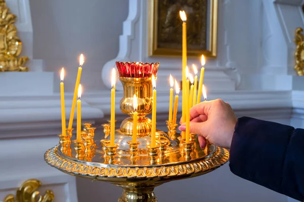 Bir kadının eli, azize dua ederken Ortodoks kilisesindeki bir ikonun önüne mum koyar. Seçici odaklanma. Yatay yönelim.
