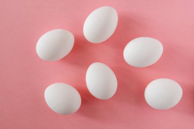 Six white eggs on a pink background.