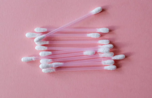 Temizlik için pamuk çubukları ve pembe arka planda plastik ve doğal pamuk lifinden yapılmış makyaj malzemesi. Plastiksiz, kozmetik konsepti. Kapatın. Yukarıdan görüntüle. 
