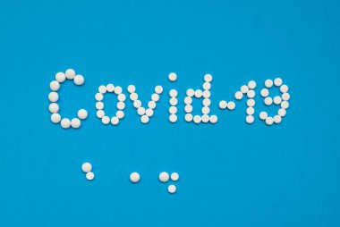 COVID-19 kelimesi, mavi arka planda beyaz tabletlerle yatay olarak yayılmış..