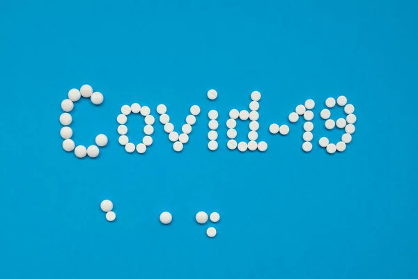La palabra COVID-19, presentada con tabletas blancas sobre un fondo azul horizontalmente . — Foto de Stock