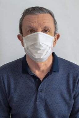 Beyaz tıbbi maskeli, gri arka planda yaşlı bir adam. Koronavirüs yüzünden endişeli. Dikey yönelim.