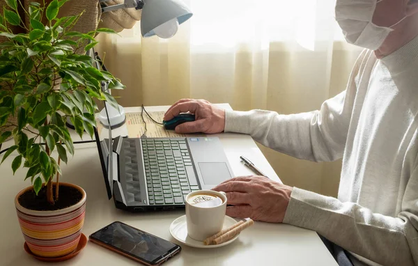 A man in a medical mask works on a computer at home. Remote work, social distancing, quarantine concept. Selective focus. horizontal orientation.