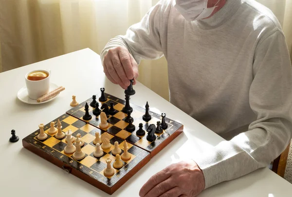 A man in a medical mask in quarantine plays chess. Quarantine, covid-19, self-isolation concept. Horizontal orientation.