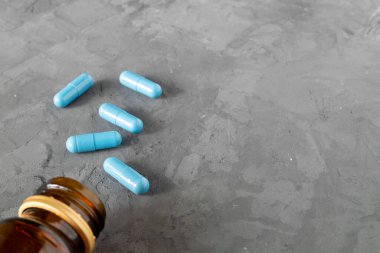 Mavi renkli tıbbi kapsüller gri arka planda duran ters dönmüş bir cam şişeden uyandı. Yatay yönelim, seçici odak, kopyalama alanı.