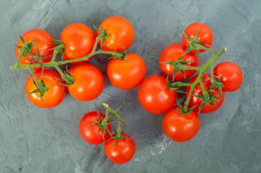 Gri bir arka planda, pürüzlü alçı desenli bir dalda kırmızı olgun domateslerin yakın çekimi. Yatay yönelim, seçici odak, üst görünüm, kopyalama alanı.