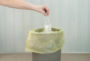 Bir kadının eli, tamamlandıktan sonra karantina sembolü olarak tıbbi maskeyi çöpe atar. Karantina sona erdi, Coperid-19 konsepti. Yatay yönelim, seçici odak.