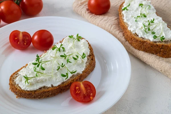 Sandwich on whole grain bread with homemade cream cheese or cottage cheese, microgreens and cherry tomatoes. Healthy food, balanced food concept. Horizontal orientation, selective focus.