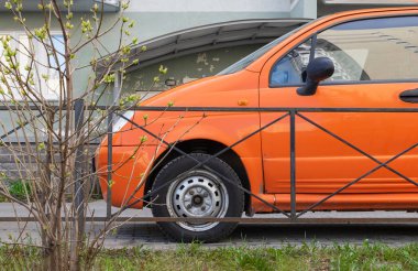 Parlak turuncu renkli küçük eski bir arabanın yakın çekimi çok katlı bir apartmanın girişine park edilmiştir. Yatay yönelim.