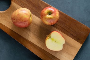 Kesme tahtasının üzerinde iki elma ve bir yarısı duruyor. Faydalı yemek, taze meyve. Yatay yönelim, yukarıdan görünüm.