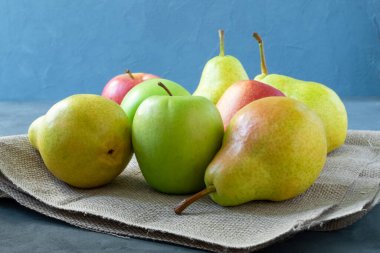 Birkaç parlak elma ve armut mavi bir arka planda basit, kaba, rustik bir peçetenin üzerinde yatıyor. Sağlıklı beslenme. Yatay yönelim, seçici odak. 