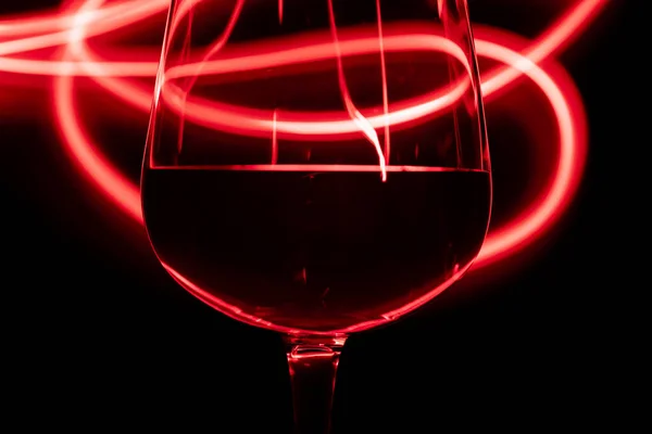Kırmızı ışık ve siyah arka planda şarap kadehinin detaylı görüntüsü.